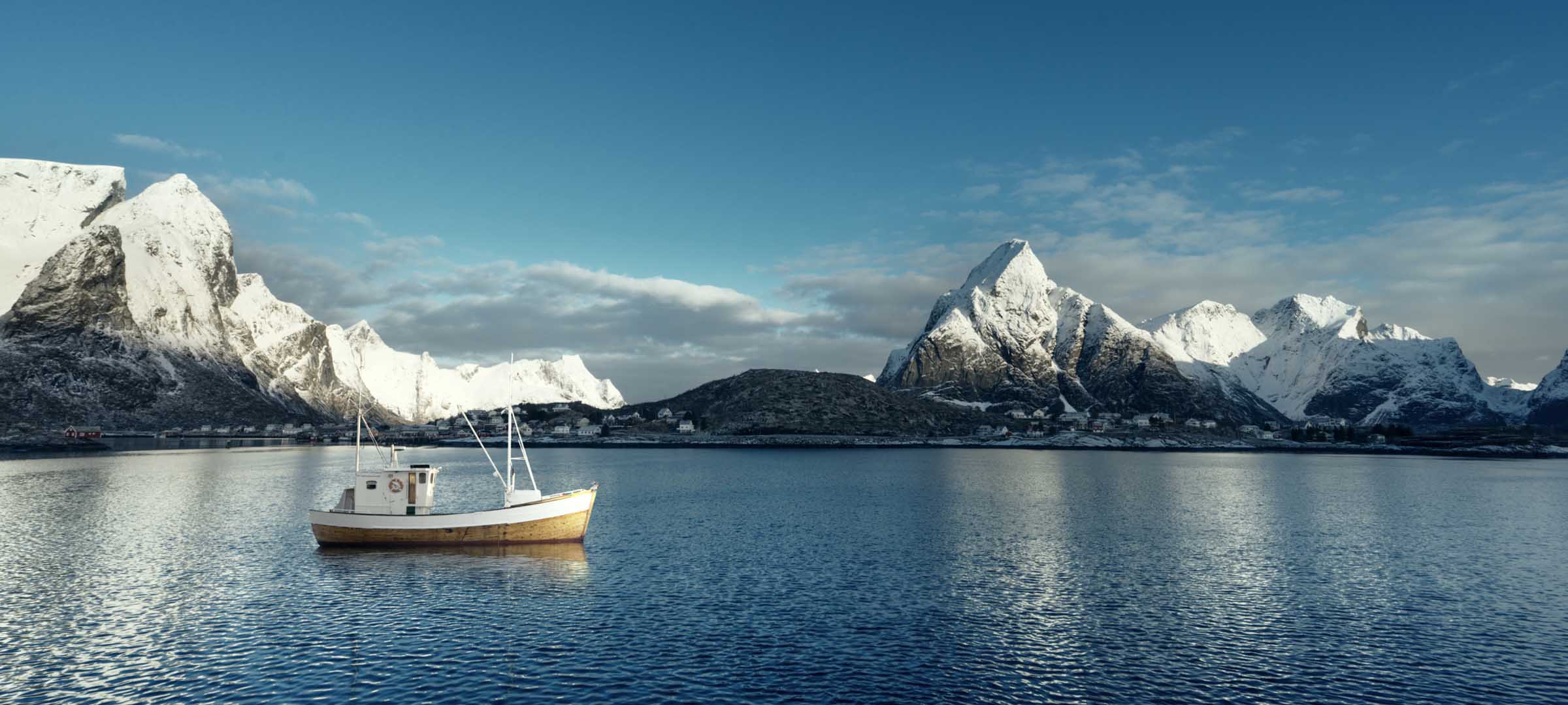 Small boat on calm water with snow-covered mountains in the background