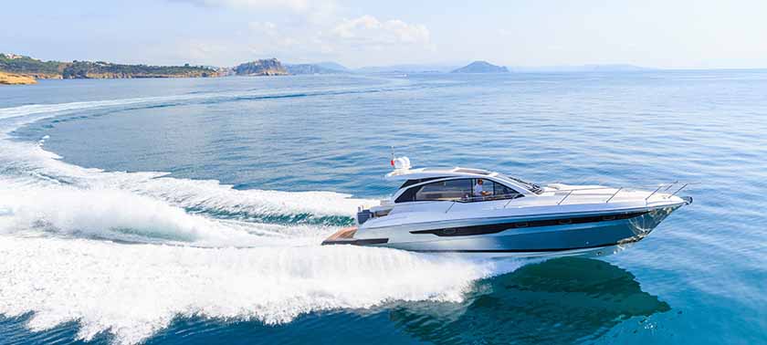 A sleek motorboat speeds through the water, leaving a trail of white foam in its wake.