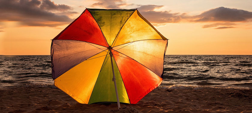 An umbrella stands on the beach, silhouetted against a vibrant sunset sky with hues of orange and purple.